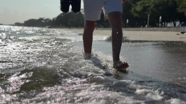 A person walks along the shoreline with gentle waves washing over his feet during early morning hours