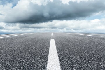 Empty asphalt road vanishing under cloudy sky.