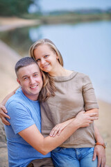 Obraz premium Summer evening. Happy and beautiful family on a walk by the river. The girl tenderly hugged her boyfriend near a large stone. Lovers. Family portrait. Husband and wife. Romantic. The guy and the girl 
