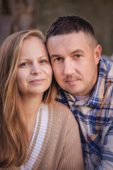Obraz premium A guy and a girl are hugging. Portrait of lovers. Warm summer evening. Husband and wife against the background of a wooden house. A man in a checkered shirt, a girl in a beige sweater. Happy family. 