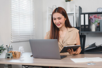 Woman working at desk with laptop and tablet in bright office setting.