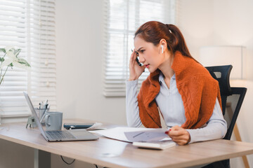 Obraz premium Woman working from home, wearing earphones, focused on laptop while talking on phone.