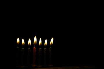 Seven Burning Candles in the Dark - Symbol of Light and Hope in Black Background