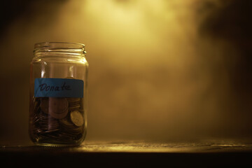 Donation Jar Filled with Coins Against Warm Golden Background - Symbol of Generosity and Charity