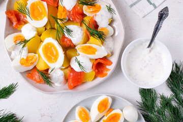Salad with smoked trout, boiled eggs, potato and sour cream sauce served on the white plate. Top view
