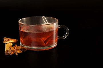 glass mug with red tea, star anise and cinnamon with black background and copy space