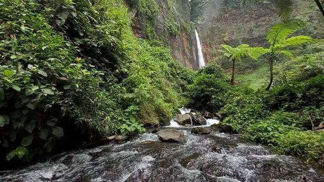 Kapas Biru waterfall seen from a distance with its clear river flow and a variety of green vegetation.