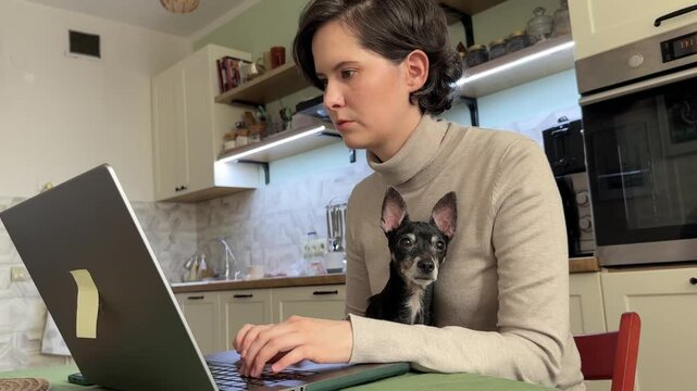 
Almaty, Kazakhstan - 02.02.2025 : A woman is sitting at her laptop, with her dog, in the kitchen. Work from home.