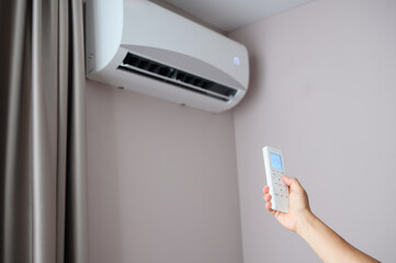 Woman holding air conditioner remote control and setting cooling temperature on split system to 17...