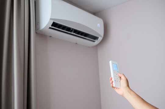 Woman holding air conditioner remote control and setting cooling temperature on split system to 17 degrees, in hotel room, at home. Concept of air cooling in hot room, climate control at home