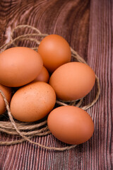 brown chicken eggs lie on a wooden surface, surrounded by rough twine.