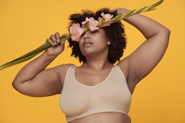 Woman with curly hair holding pink flowers against her face while closing her eyes and stretching...