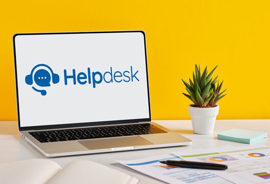 Laptop displaying helpdesk software on a desk with documents and plant