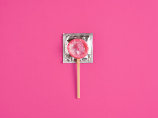 Pink condom on wooden stick placed on pink background. Safe sex, sexual health and pleasure concept.