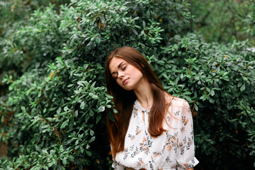 Frustrated young woman leaning against bush with eyes closed in moment of contemplation and distress