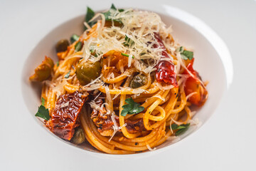 Spaghetti or Putanessa pasta according to a traditional Italian recipe with anchovies, olives, capers and tomatoes on a white plate. Close-up. Space for text.