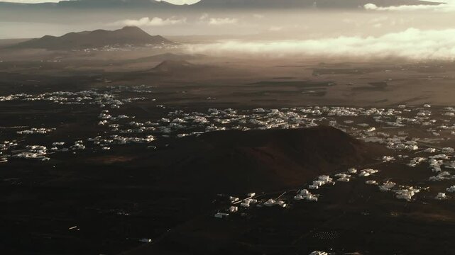 Lev&eacute; du soleil dans un paysage lunaire &agrave; Lanzarote dans les &Icirc;les Canaries avec vues a&eacute;rienne sur des maisons blanches typiques, des volcans et des montagnes. Dunes noire et nuages en arri&egrave;re plan. 