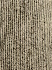 Close-up of textured sand with evenly spaced ripples formed by wind or water. The surface showcases natural patterns and small grains, creating a minimalist and abstract background.