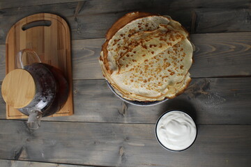 Crepe pancakes on a plate with white sauce, yogurt, sour cream on a gray background, top view. Concept of the holiday Maslenitsa meeting spring