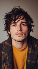 Obraz premium Charming young man with tousled hair and a stylish plaid coat poses against a neutral backdrop, exuding confidence and warmth