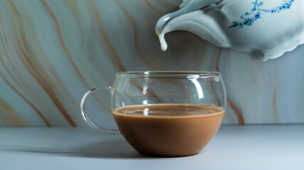 Pouring milk into a glass cup of tea against a softly marbled background in a cozy setting