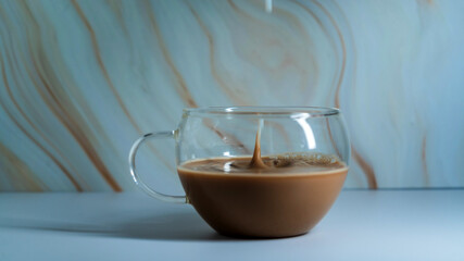 Warm beverage being poured into a transparent glass cup against a textured marble background