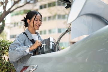 A smiling Asian woman places her luggage in the trunk of a car, getting ready for her trip.