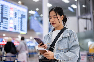 A positive, thoughtful Asian female passenger checks her flight boarding time on her smartphone.
