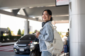 A beautiful Asian female traveler stands at an airport pickup point, waiting for a taxi. © bongkarn