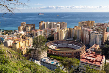 Photo of the streets of the city of Malaga in Spain showing the famous old historic bull fighting ring arena surrounded by high rise apartment blocks with the ocean in the background on a sunny day
