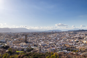 Photo of the streets of the city of Malaga in Spain showing an aerial view of the city centre with the high rise apartments and mountains in the background on a sunny day in the month of January