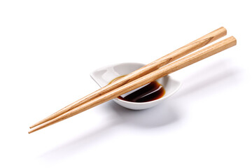 Wooden chopsticks elegantly placed beside a small bowl of soy sauce on a clean white background