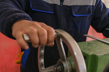 A factory worker operating a manual handwheel on an industrial machine, adjusting precision...