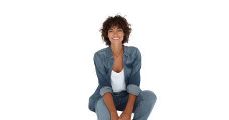 Beautiful tanned woman with curly hair in denim attire poses playfully in a bright studio setting, showcasing fashion and personality with a radiant smile