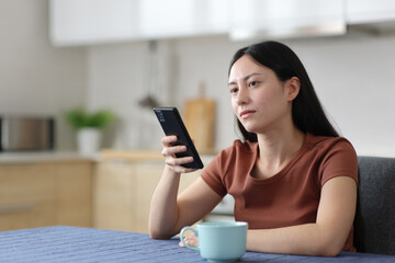 Distracted asian woman holding phone in the kitchen