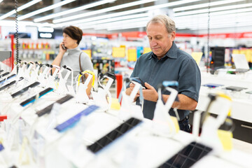 Older man picking out new phone to buy in electronics department of supermarket
