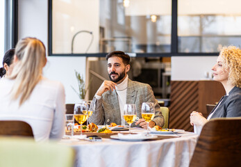 Portrait of businessman sitting with coworkers in restaurant, talking during business lunch.