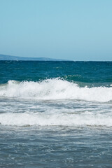 Waves gently lap against the shore on a sunny day at a tranquil beach. vertical