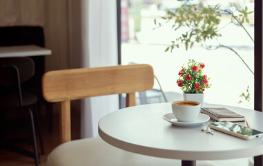 Fototapeta premium Latte coffee with mobile phone and note book on white table by the window, relax in the morning in cafe before work