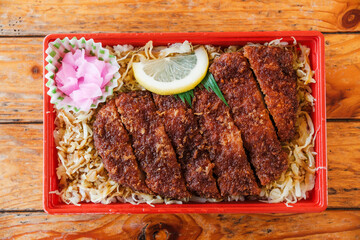 Japanese train bento box featuring crispy tonkatsu (breaded pork cutlet) over shredded cabbage and rice, served with pickled ginger and lemon slice. Tasty traditional meal, captured in Tokyo, Japan