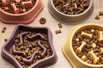 Different shapes of slow feeder bowls with dry food for dogs on wooden surface