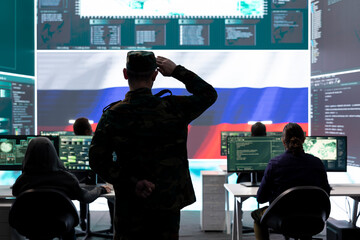Russian military soldier presenting the official salute in monitoring room, inflicting propaganda and misinformation among the population. Hackers spreading fake news during conflict.