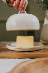 A butter knife is on top of a butter dish. The butter dish is white and has a lid