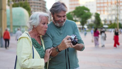 Elderly couple enjoys learning photography together, navigating a vintage camera in a vibrant city square - Powered by Adobe