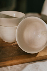 Four white bowls are sitting on a wooden cutting board. The bowls are all different sizes and are arranged in a row. The wooden cutting board is the background of the image