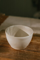 A white bowl sits on a wooden table. The bowl is empty and has a simple, clean design. The table is made of wood and has a natural, rustic feel. The scene is calm and peaceful
