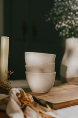 Three white bowls sit on a wooden table next to a candle. The bowls are empty and the candle is lit. The scene has a cozy and warm atmosphere, with the candle providing a soft glow