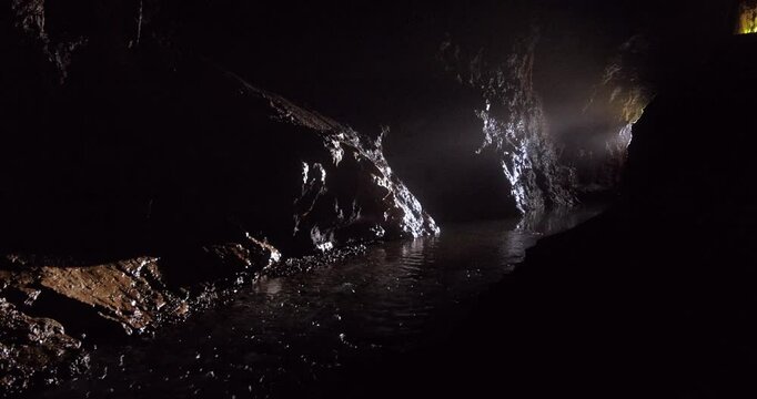 A serene view of an underground river flowing through the dark chambers of Prometheus Cave in Georgia. The shimmering light reflects off the wet stone walls, creating a mystical yet atmosphere