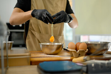 Male baker cracking an egg into mixing bowl preparing ingredients for homemade cookies