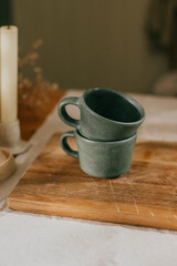 Two green cups on a wooden cutting board. The cups are sitting on top of the board and are not in use